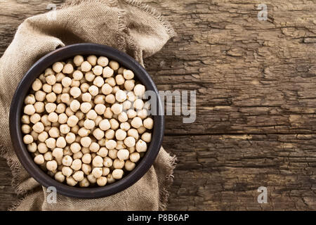 Roh Kichererbsen oder kichererbsebohnen (lat. Cicer arietinum) im rustikalen Schüssel, Overhead auf rustikalem Holz mit Kopie Platz auf der Seite fotografiert. Stockfoto