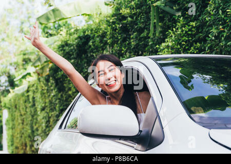 Junge asiatische Frau glücklich lächelnd und winkend vom Fahrersitz im Auto während der Einnahme auf Reise Stockfoto