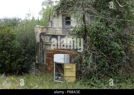 Verlassenes Haus überlaufen durch Natur und verworfen, der Kühlschrank im Garten mit Pflanzen bewachsen. Stockfoto