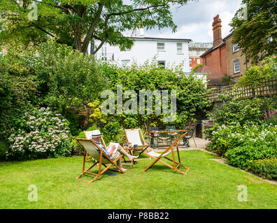 Ältere Mann, der Panama Hut Lösung Kreuzworträtsel im Liegestuhl sitzen im großen Garten in Sommerhitze, London, England, Großbritannien Stockfoto