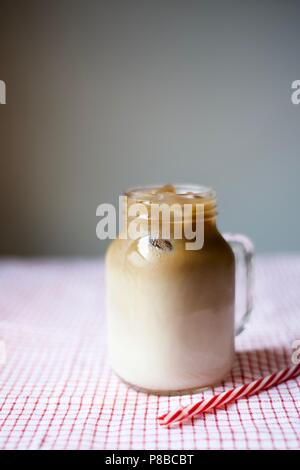 Eiskaffee in einem Marmeladenglas Tasse mit einem Strohhalm auf Tischdecke auf grauem Hintergrund, Sommer trinken, trinken Konzept Stockfoto