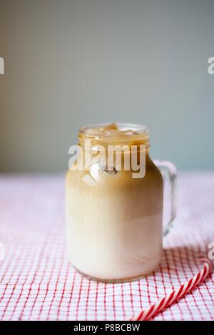 Eiskaffee in einem Marmeladenglas Tasse mit einem Strohhalm auf Tischdecke auf grauem Hintergrund, Sommer trinken, trinken Konzept Stockfoto