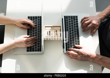 Blick von oben auf die männliche und weibliche Hände zwischen Drucken auf Laptops mit Holz- Kalender Stockfoto