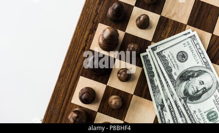 Zugeschnittenes Bild von Schachbrett mit Bargeld und schwarzen Schachfiguren auf weiße Oberfläche Stockfoto