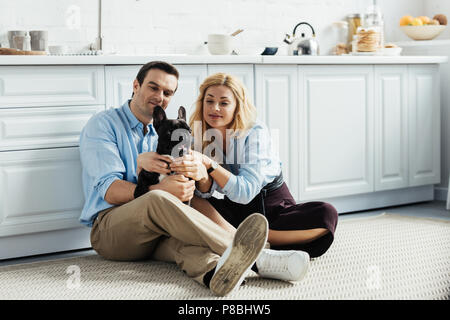 Lächelndes Paar ihre Französische Bulldogge Streicheln auf Küche Etage Stockfoto