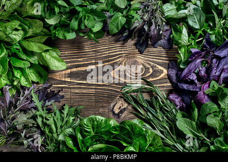 Auswahl an frischen Kräutern auf Holz- Hintergrund. Frisch geerntete Kräuter wie Basilikum, Rucola. Ansicht von oben. Kopieren Sie Platz. Stockfoto