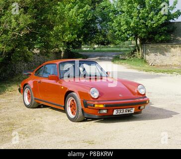 Porsche 911 Carrera 3.2 1985 Modell Jahr - in der Garde rote Farbe gezeigt, Vorder- und Seitenansicht in ländlicher Umgebung Stockfoto