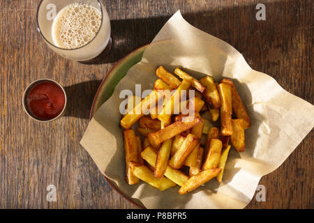 Teller Pommes Frites mit Ketchup und Glas dunkles Bier auf Holztisch, Nahaufnahme, Ansicht von oben Stockfoto