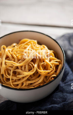 Nahaufnahme von einem weißen Keramik Schüssel mit Yakisoba Nudeln mit Gemüse und Sauce yakisoba, auf einem weißen rustikalen Holztisch Stockfoto