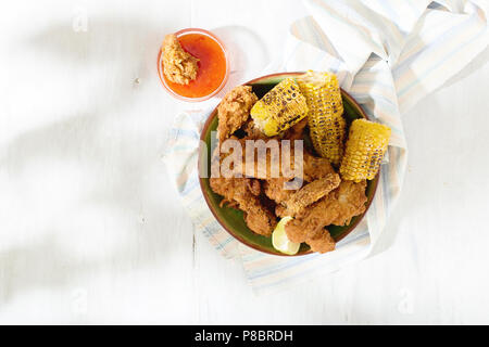 Fried Chicken leg in der Platte auf weissem Holztisch mit gegrilltem Mais und roten pikanter Sauce, Ansicht von oben Stockfoto