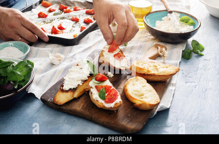 Nahaufnahme der männlichen Händen kochen Italienisch Bruschetta mit Tomaten, Basilikum und Käse Stockfoto