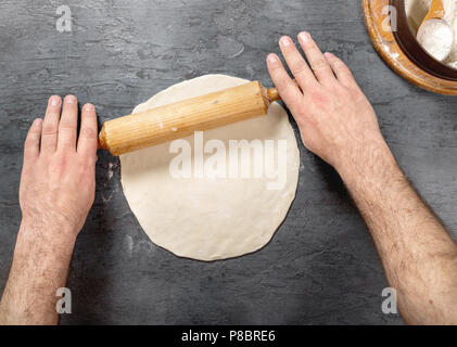 Mann Vorbereitung Pizza Teig auf dunklen Untergrund in einer Bäckerei Nahaufnahme, Ansicht von oben Stockfoto