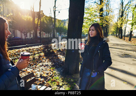 Zwei Freundinnen im Herbst Kleidung sprechen auf der Straße und trinken Kaffee Stockfoto