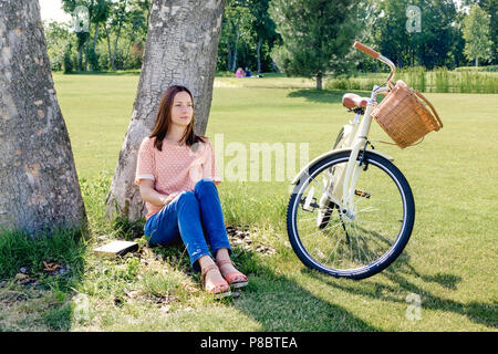 Schöne unbeschwerte Frau sitzt unter einem Baum genießen den Moment im Sommer Stockfoto