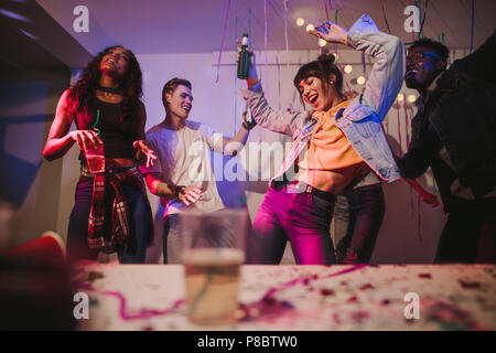 Junge Männer und Frauen, die Spaß an einem bunten House Party. Freunde tanzen in Freude holding Getränke an einer Party. Stockfoto