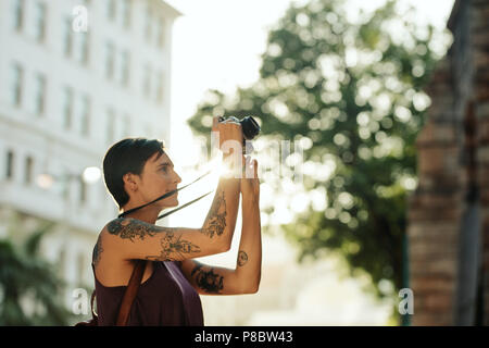 Frau Reisenden, Fotos mit Ihrer Kamera mit Sonne in den Hintergrund. Tourist mit Tattoo auf der Hand gehen, um die Stadt herum Fotografieren Stockfoto