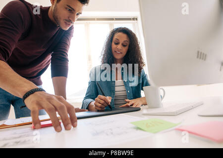 Geschäftsmann auf Geschäftspapieren, während die Frau schreiben auf der digitalen Schreibblock ist. Business Partner zusammen arbeiten im Büro. Stockfoto