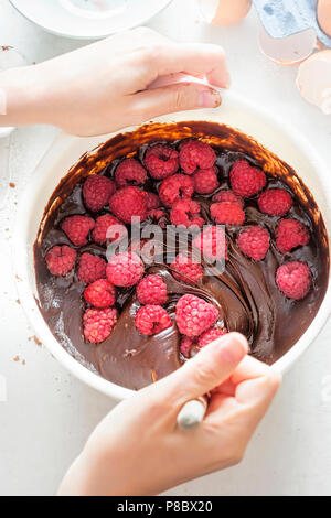 Weibliche Hände mischen Himbeeren mit Chocolate brownies Teig in weiße Schüssel Stockfoto