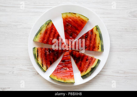 Scheiben frische reife gegrillter Wassermelone auf einer weißen Platte über weiße Holz- Hintergrund, Ansicht von oben. Gesund sommer Bio-obst. Stockfoto