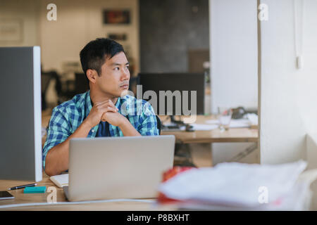 Asiatische Designer an seinem Schreibtisch sitzen tief in Gedanken Stockfoto