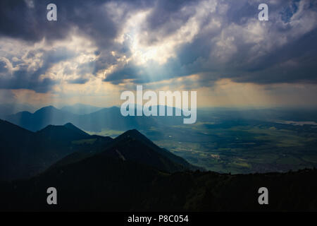 Sonnenstrahlen leuchten hell durch dunkle und schwere Wolken über die Berge und Landschaft ein Gewitter Atmosphäre Gipfel der Bayerischen Alpen in der Nähe München Stockfoto