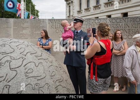 Auf das 100-jährige Jubiläum der Royal Air Force (RAF) und nach einer Flypast von 100 Flugzeugen Formationen, die die britische Luftverteidigung Geschichte die über Central London flog, ein Veteran hält sein Kind neben dem Denkmal für die in der Bombenanschlag von Bali 2002 getötet, am 10. Juli 2018 in London, England. Stockfoto