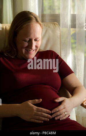 Blonde Dame in der Mitte der 30er Jahre sitzen und streichelte ihren schwangeren Bauch. Stockfoto