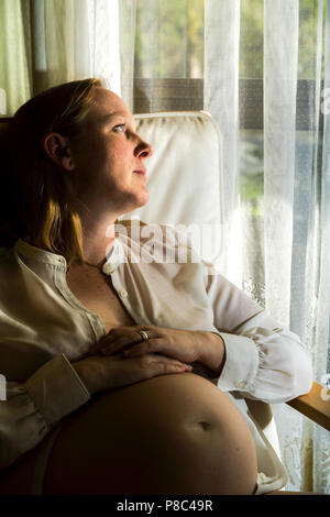 Blonde Dame in der Mitte der 30er Jahre sitzen und streichelte ihren schwangeren Bauch. Stockfoto