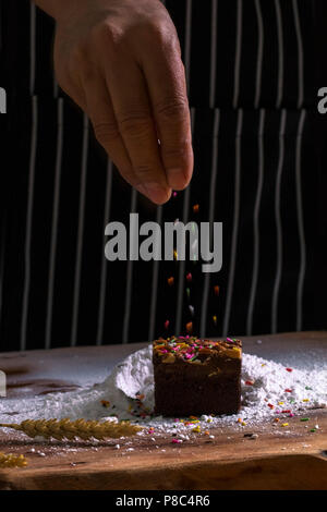 Chef's Hände besprengung Chocolate Brownie mit Puderzucker und Mehl Sichter auf Hintergrund. Kopieren. Stockfoto