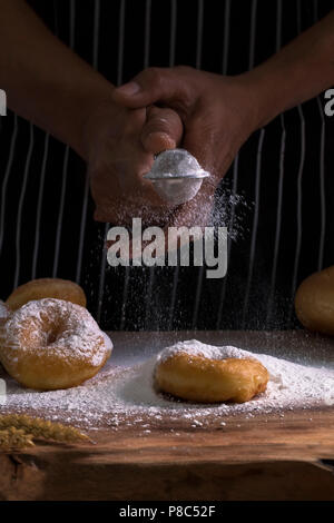 Chef's Hände Besprengung süße Krapfen mit Puderzucker und Mehl Sichter auf Hintergrund. Kopieren. Stockfoto