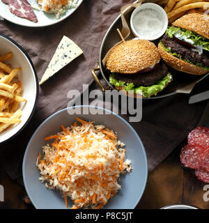 Köstliche Tisch im Freien mit Burger, Pommes, Salate und Snacks auf Holztisch, Ansicht von oben. Im Freien essen Konzept Stockfoto