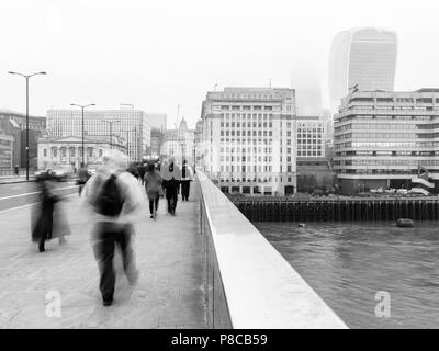 Montag morgen Pendler gehen auf die London Bridge über der Themse und gegenüber der City und Walkie Talkie Gebäude auf einem nebligen Tag arbeiten. Stockfoto