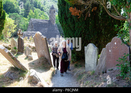 Glendalough, Wicklow, Irland. 10. Juli 2018: Touristen, die in der Glendalough Tal mit seinen berühmten Kloster an einem sonnigen Dienstag Nachmittag. Stockfoto