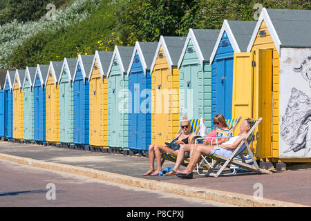 Bournemouth, Dorset, Großbritannien. 11. Juli 2018. UK Wetter: Ein anderes heißen, sonnigen Tag in Bournemouth mit kein Zeichen der Hitzewelle noch beenden, als Sonnenanbeter Kopf ans Meer in Bournemouth Strände. Drei Frauen Sonnen in Liegestühlen außerhalb einer Reihe der Umkleidekabinen am Strand an der Promenade. Credit: Carolyn Jenkins/Alamy leben Nachrichten Stockfoto