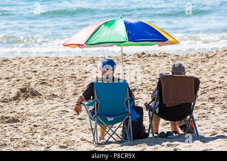 Bournemouth, Dorset, Großbritannien. 11. Juli 2018. UK Wetter: Ein anderes heißen, sonnigen Tag in Bournemouth mit kein Zeichen der Hitzewelle noch beenden, als Sonnenanbeter Kopf ans Meer in Bournemouth Strände. Paar sitzen auf Stühlen unter bunten Sonnenschirm genießen den Sonnenschein. Credit: Carolyn Jenkins/Alamy leben Nachrichten Stockfoto