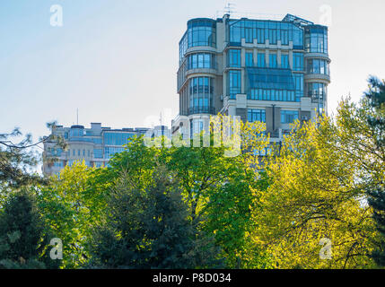 Hohes Gebäude mit vielen Fenstern und Balkonen aus Glas auf dem Hintergrund der Wipfel der Bäume mit gelbem und grünem Laub. Für ihr Design Stockfoto