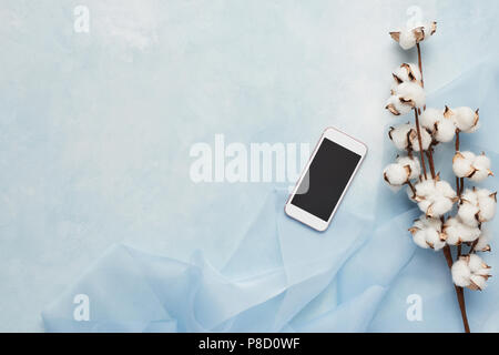 Flach Konzept der weiblichen Hellblauer Hintergrund mit Handy, Seide und Zweig der künstlichen Baumwolle Blume. Ansicht von oben mit der Kopie. Stockfoto