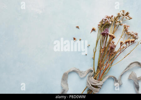 Flach Konzept der weiblichen Hellblauer Hintergrund mit getrockneten Wildblumen gebunden mit Seide. Ansicht von oben mit der Kopie. Stockfoto
