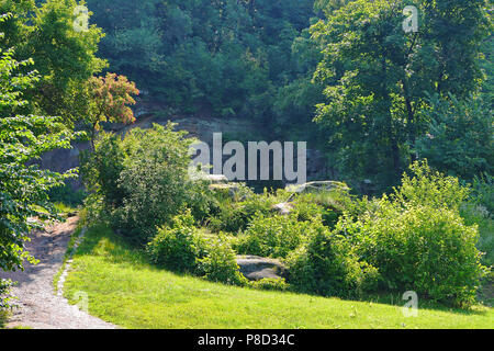 Eine malerische Landschaft der Natur mit großen Felsbrocken liegen unter den Büschen neben der steinernen Mauer und Bäume wachsen. . Für ihr Design Stockfoto