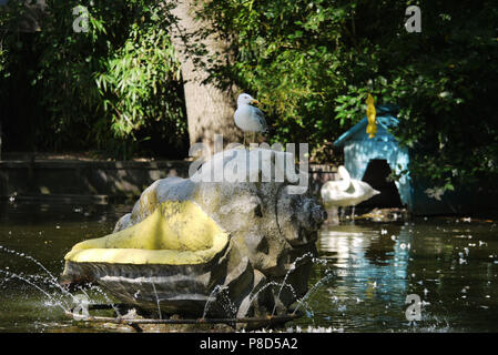 Eine Möwe auf einer großen Schale einer Statue mit einem Brunnen auf einem See in der Nähe des Swan im Hintergrund. Für ihr Design Stockfoto