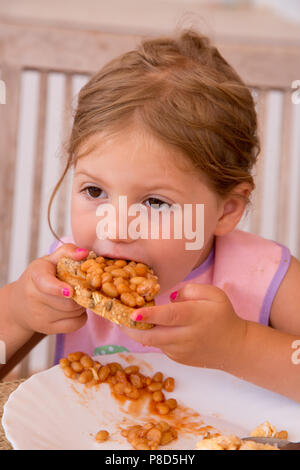 Ein Mädchen von zwei Einhalb Essen gebackene Bohnen auf Toast mit Rührei Stockfoto