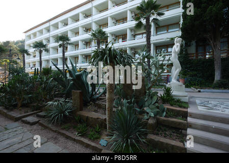 Fünfstöckiges Hotel in Weiß mit Palmen und einer Statue im Vordergrund. Für ihr Design Stockfoto