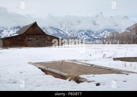 Ein kleiner Steg führt zum moulton Scheune auf einem kalten Wintertag. Der Grand Teton National Park, Wyoming Stockfoto