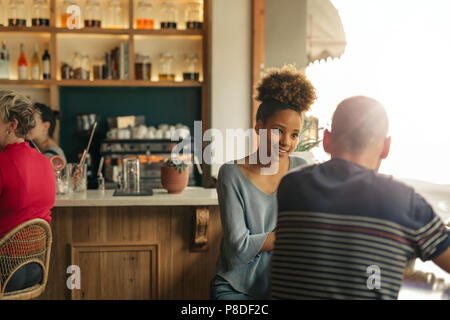 Lächelnde junge Frau im Gespräch mit ihrer Freundin in einer Bar Stockfoto