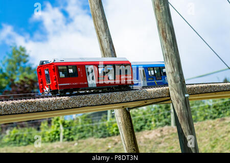 Zwei Lokomotiven Spielzeug, eine blaue und eine rote, auf einer Holzbrücke. Blauen Himmel im Hintergrund Stockfoto