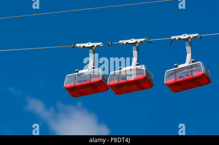 Drei rote Spielzeug Seilbahnen auf dem Seil. Himmel im Hintergrund Stockfoto
