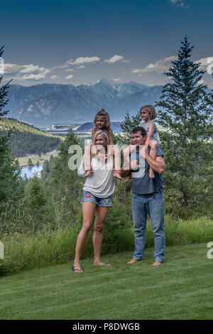 Attraktive, Verspielt, lässig Family Portrait von Eltern und zwei kleinen Töchtern. Hat jeder Elternteil Kind auf sholders, in einem im Freien. Model Release Stockfoto