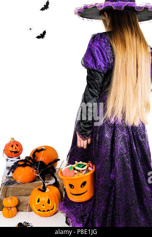 Mädchen in eine Hexe, Kleid mit Halloween Zubehör und vollen Eimer Süßigkeiten auf isolierten Hintergrund Stockfoto