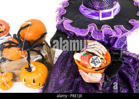 Mädchen in eine Hexe, Kleid mit Halloween Zubehör und vollen Eimer Süßigkeiten auf isolierten Hintergrund Stockfoto