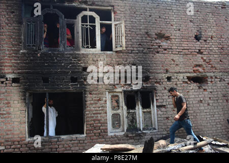 Shopian, Indien. 10. Juli 2018. Leute schauen auf die beschädigte Wohnhaus in Shopian Distrikt des indischen verwalteten Kaschmir am 10. Juli 2018. Zwei Rebellen nämlich Sameer Ahmad Sheikh lokaler und Babar aus Pakistan in eine Begegnung mit indischen Truppen in Shopian Bezirk von Kaschmir getötet wurden. Eine der Zivilisten Tamsheel Khan ein 18 Jahre alter Junge auch sein Leben verlor, als er während der Proteste rund um den Gun battle Seite geschossen wurde und viele verletzt worden. Credit: Muzamil Mattoo/Pacific Press/Alamy leben Nachrichten Stockfoto